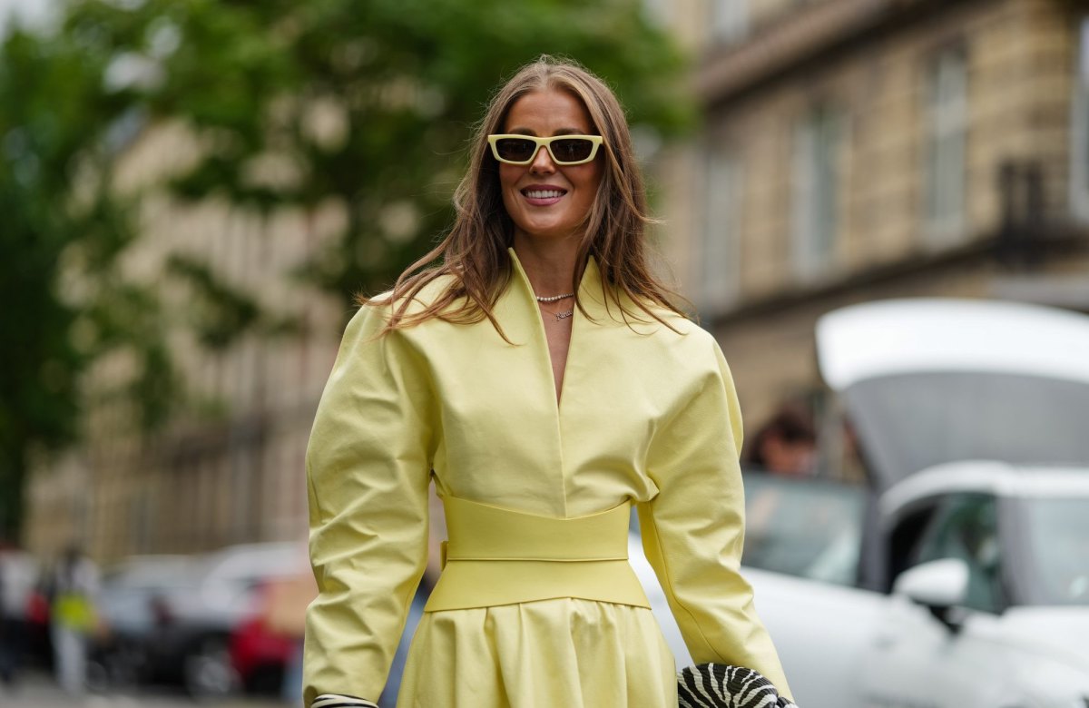 COPENHAGEN, DENMARK - AUGUST 04: Nina Sandbech wears a light yellow dress with a structured, high neckline and long sleeves. The dress features a fitted waist and midi-length skirt accentuated by a large yellow leather belt and a flared. Sunglasses with a matching yellow frame are worn. A black and white patterned clutch is held in one hand. The outfit is accessorized with gold bracelets on the wrist. Black and white zebra-patterned heels complete the ensemble, outside OperaSport, during Copenhagen Fashion Week, on August 04, 2025 in Copenhagen, Denmark (Photo by Edward Berthelot/Getty Images)