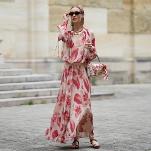 MUNICH, GERMANY - MAY 29: Marlies Pia Pfeifhofer is seen wearing a light beige silk chiffon long sleeve maxi dress with red and pink prints of feathers and flowers, drawstring waist, deep V-neck with front tie and smocking details on the collar and cuffs from FENDI, a natural-colored Baguette canvas bag with coral bandana embroidery, small fringes on the flap, calfskin leather straps, golden hardware and logo detail as well as an additional golden chain metal charm with marine-inspired pendants and a red, pink and white bandana charm with golden logo clip from FENDI, a pair of chocolate brown leather gladiator sandals with a braided leather toe strap and one main strap from Alex Rivière x Manebi, a Louis Tortoise Brown sunglasses with slim and oval shape from Corlin, a gold-colored metal and brown nappa leather Forever Fendi necklace with shell-shaped pendants from FENDI, a brown leather Tank Louis watch with yellow gold rectangular watch case from Cartier, a silver diamond ring on May 29, 2025 in Munich, Germany. (Photo by Moritz Scholz/Getty Images)