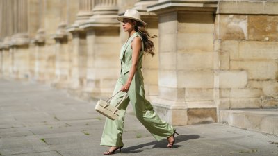 Angela Gonzalez wears a beige suede Lack Of Color hat, earrings, a black off shoulder top, a pale green buttoned blazer jacket sleeveless from Nasty Gal, pale green matching Nasty Gal flared pants, a gold chain bracelet, a beige shiny leather Mango handbag, brown shiny leather strappy hells Na-Kd sandals, on May 29, 2021 in Paris, France.