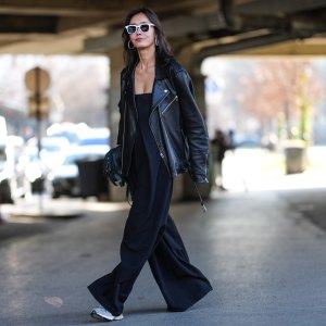 PARIS, FRANCE - MARCH 05: A guest wears white sunglasses, silver hoop earrings, shiny black oversized leather jacket, shiny black leather bag, black sleeveless flowy romper, light gray sneaker shoes, outside Stella McCartney, during the Paris Fashion week Women's Fall/Winter 2025-2026 on March 5, 2025 in Paris, France. (Photo by Edward Berthelot/Getty Images)