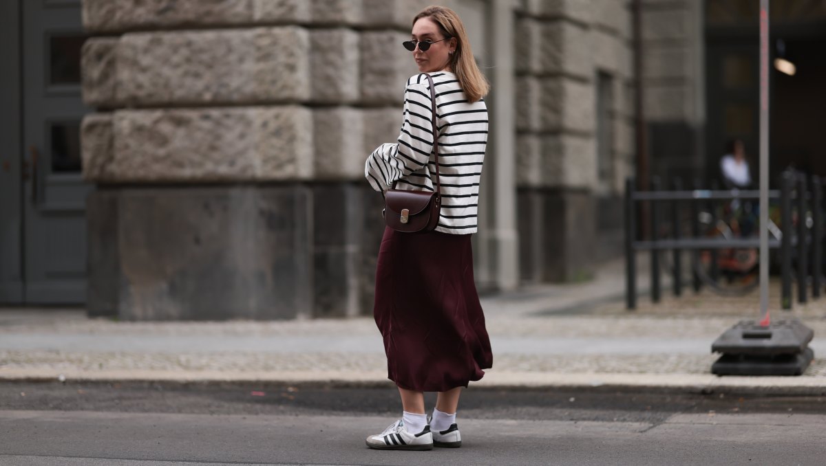 BERLIN, GERMANY - JULY 13: Sonia Lyson is seen wearing several silver and golden earrings and ear studs; a black, oval sunglasses with filigree metal frame from Yves Saint Laurent; a white sweatshirt with black stripes and loose fit from Zara; a burgundy satin midi skirt from Zara; a burgundy leather bag from Sézane; white socks and white Samba sneakers from Adidas on July 13, 2024 in Berlin, Germany. (Photo by Jeremy Moeller/Getty Images)