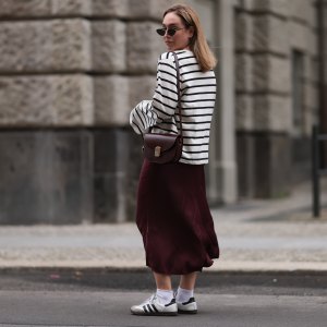 BERLIN, GERMANY - JULY 13: Sonia Lyson is seen wearing several silver and golden earrings and ear studs; a black, oval sunglasses with filigree metal frame from Yves Saint Laurent; a white sweatshirt with black stripes and loose fit from Zara; a burgundy satin midi skirt from Zara; a burgundy leather bag from Sézane; white socks and white Samba sneakers from Adidas on July 13, 2024 in Berlin, Germany. (Photo by Jeremy Moeller/Getty Images)