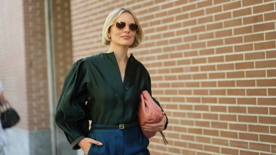 Violet Grace Atkinson wears a chin-length straight blonde bob with a center part, gold-framed brown-lens sunglasses, small gold stud earrings, a pink slouchy leather pouch bag, a dark green satin blouse with a slight stand collar, concealed front buttons and voluminous puff long sleeves, a thin black leather belt from Fendi with a gold-tone buckle and high-waisted teal satin wide-leg trousers, outside Fendi, during Milan Fashion Week - Womenswear Spring/Summer 2026, on September 24, 2025 in Milan, Italy