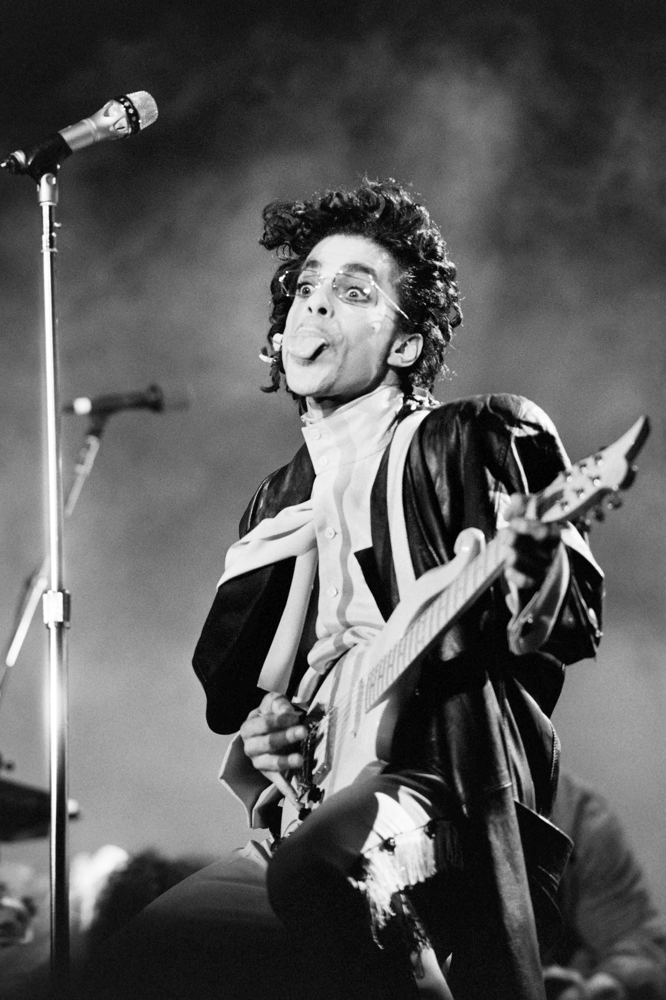 Prince sticking out his tongue on stage while playing guitar.