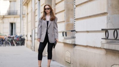 PARIS, FRANCE - APRIL 21: Merve Gorgoz wears long, wavy light brown hair parted at the center, natural makeup with defined brows and nude lipstick, amber colored rectangular Saint Laurent sunglasses, a taupe gray LilySilk oversized blazer jacket with notched lapels and front button fastening layered over a black top, black Massimo Dutti cropped capri pants, a black Saint Laurent leather clutch bag, and black Studio Amelia strappy high heel shoes, during a street style fashion photo session, on April 21, 2026 in Paris, France. (Photo by Edward Berthelot/Getty Images)