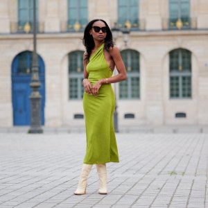 PARIS, FRANCE - APRIL 29: Emilie Joseph wears black large sunglasses, micro crystal earrings, a green satin / silk asymmetric one strap shoulder midi tube dress, gold bracelets, pale yellow shiny leather block heels knees boots / high boots , during a street style fashion photo session, on April 29, 2023 in Paris, France. (Photo by Edward Berthelot/Getty Images)