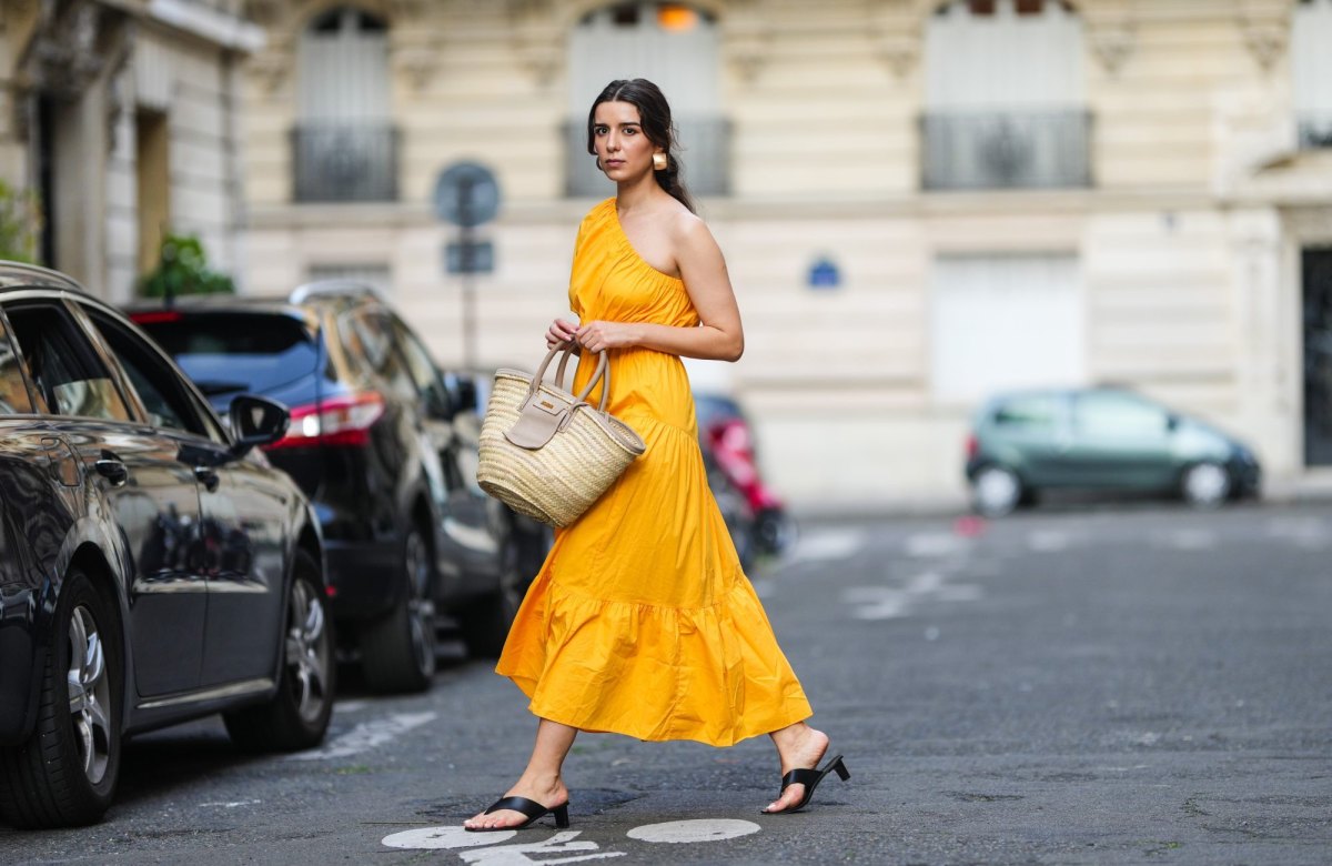 PARIS, FRANCE - AUGUST 12: Ketevan Giorgadze @katie.one wears a one shoulder cut out maxi dress in orange from Mango, oversized golden hoop earrings from Zara, flip flop heeled black sandals shoes from APC Paris, a Le Grand Panier beach straw bag by Jacquemus, on August 12, 2021 in Paris, France. (Photo by Edward Berthelot/Getty Images)