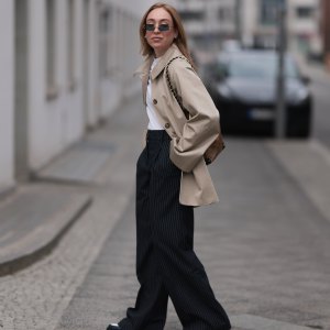 BERLIN, GERMANY - MARCH 24: Sonia Lyson seen wearing Linda Farrow black rectangular sunglasses with dark lenses, adding a modern and edgy touch, Sézane classic white crew-neck cotton t-shirt, Sézane beige oversized trench coat with large statement buttons and a relaxed fit, Sézane high-waisted black pinstriped wide-leg trousers, Louis Vuitton brown logo monogram pattern bucket bag with gold chain straps adds a sophisticated contrast and Sézane black-and-white leather platform loafer shoes with a chunky sole, on March 24, 2025 in Berlin, Germany. (Photo by Jeremy Moeller/Getty Images)