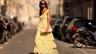Emilie Joseph @in_fashionwetrust wears black sunglasses, a pale yellow with green and yellow flower print pattern V-neck / tank-top / backless / belted / ruffled maxi long dress, a beige fabric ruffled clutch, silver rings, pale yellow matte leather pointed pumps heels shoes, during a street style fashion photo session, on March 26, 2022 in Paris, France.