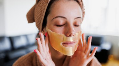 A beautiful woman pressing a sheet mask onto her face - stock photo