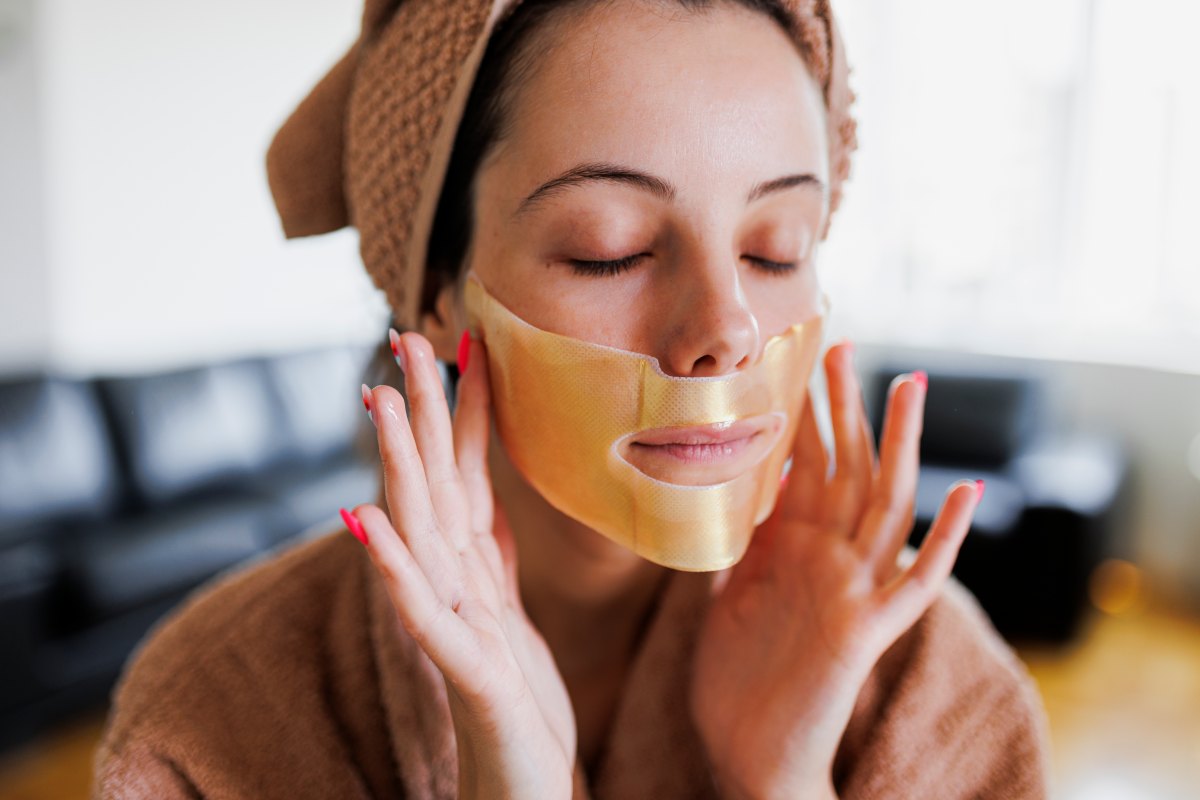 A beautiful woman pressing a sheet mask onto her face - stock photo