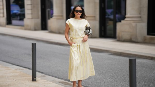 Laura Noltemeyer is seen wearing a yellow striped two-piece set with a sleeveless draped top and matching midi skirt by Sézane; black flip-flop sandals by Amazon; a black-and-white striped Porter clutch bag; black cat-eye sunglasses by Saint Laurent; nude-colored fingernails and toenails; gold jewelry by H&M and COS consisting of earrings, bangles and rings; natural makeup; her dark brown hair is worn in soft waves with a middle part on May 5, 2026 in Hamburg, Germany.