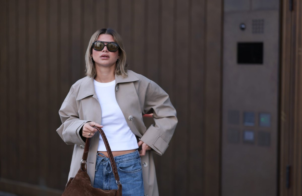BERLIN, GERMANY - APRIL 01: Sophia Geiss seen wearing Vehla Eyewear black / brown dark sunglasses, Drykorn white cotton basic casual cropped top, Meotine beige oversized trench coat adds effortless elegance, COS blue denim oversized, loose-fitting, wide-leg jeans with a drawstring waist enhance the relaxed vibe and a brown suede leather vintage bag complements the western aesthetic, on April 01, 2025 in Berlin, Germany. (Photo by Jeremy Moeller/Getty Images)