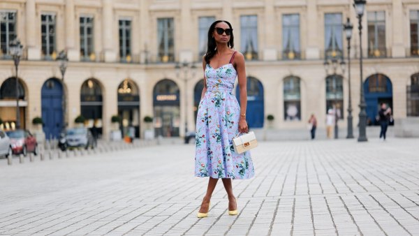 PARIS, FRANCE - APRIL 29: Emilie Joseph wears black large sunglasses, crystal earrings, a pale blue with red / green / navy blue / beige flower print pattern heart neck / tank-top / belted / midi dress, gold bracelets, a beige wickers and white shiny leather bi-material handbag, yellow shiny leather pointed pumps heels shoes , during a street style fashion photo session, on April 29, 2023 in Paris, France. (Photo by Edward Berthelot/Getty Images)