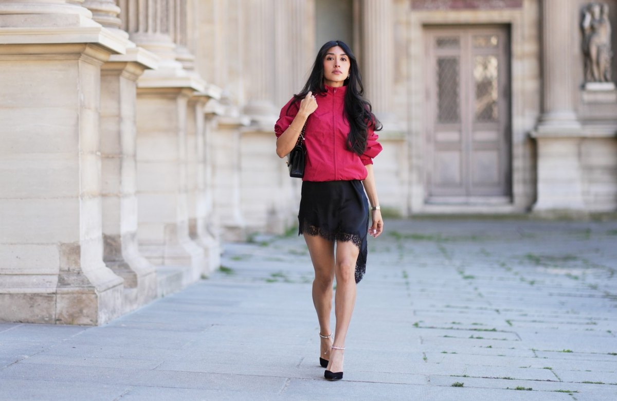 PARIS, FRANCE - APRIL 24: Angela Gonzalez wears long wavy black hair, a red windbreaker jacket by Zara, a black lace-trim mini dress by Zara, a black leather bag by Chanel, black ankle-strap pumps crystal embellished shoes by Jimmy Choo, during a street style fashion photo session, on April 24, 2026 in Paris, France. (Photo by Edward Berthelot/Getty Images)