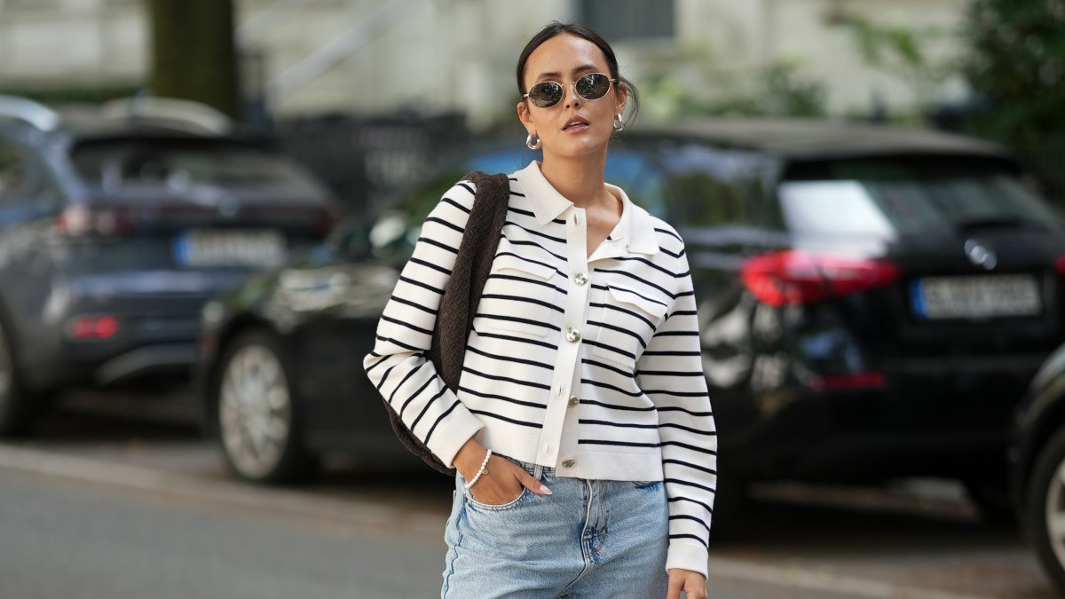 HAMBURG, GERMANY – AUGUST 17: Laura Noltemeyer is seen wearing a cream-and-navy striped knit cardigan with pearl buttons from Sézane; styled with light blue high-waisted straight-leg jeans with frayed hems from Zara; paired with taupe suede loafers from Birkenstock; is carrying a chocolate-brown woven leather shoulder bag from Les Visionnaires; accessorized with round metal-frame sunglasses from Persol and a delicate silver bracelet. Her hair is parted in the middle and styled in a sleek low ponytail on August 17, 2025 in Hamburg, Germany. (Photo by Moritz Scholz/Getty Images)