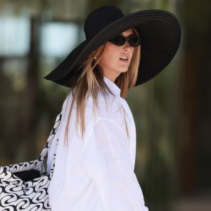 COPENHAGEN, DENMARK - AUGUST 06: A fashion week guest is seen wearing a white long-sleeved shirt, a white oversized shirt with wide sleeves and white shorts, an oversized black hat, an oversized patterned bag with white and black graphics and black sandals before OperaSport show during day two of the Copenhagen Fashion Week (CPHFW) SS25 on August 06, 2024 in Copenhagen, Denmark. (Photo by Jeremy Moeller/Getty Images)