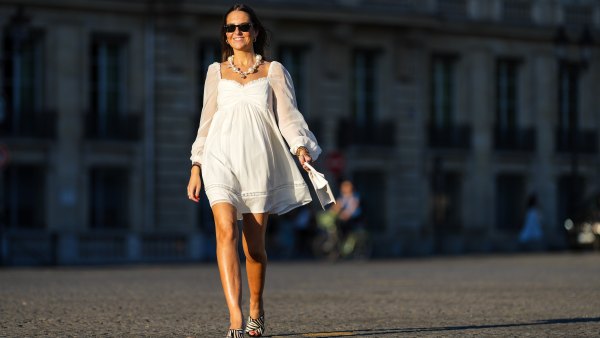 Alba Garavito Torre wears black sunglasses from Ray Ban, a white baby doll mini dress with ruffled sweetheart neckline / sheer blouson sleeves and a crystal and lace insert from Kismet Studios, a white Chiquito handbag from Jacquemus, black and white zebra print pattern heels mules / sandals with squared toe and mid heel from Brooklyn Bandit, gold bracelets, during a street style fashion photo session, on July 31, 2022 in Paris, France.