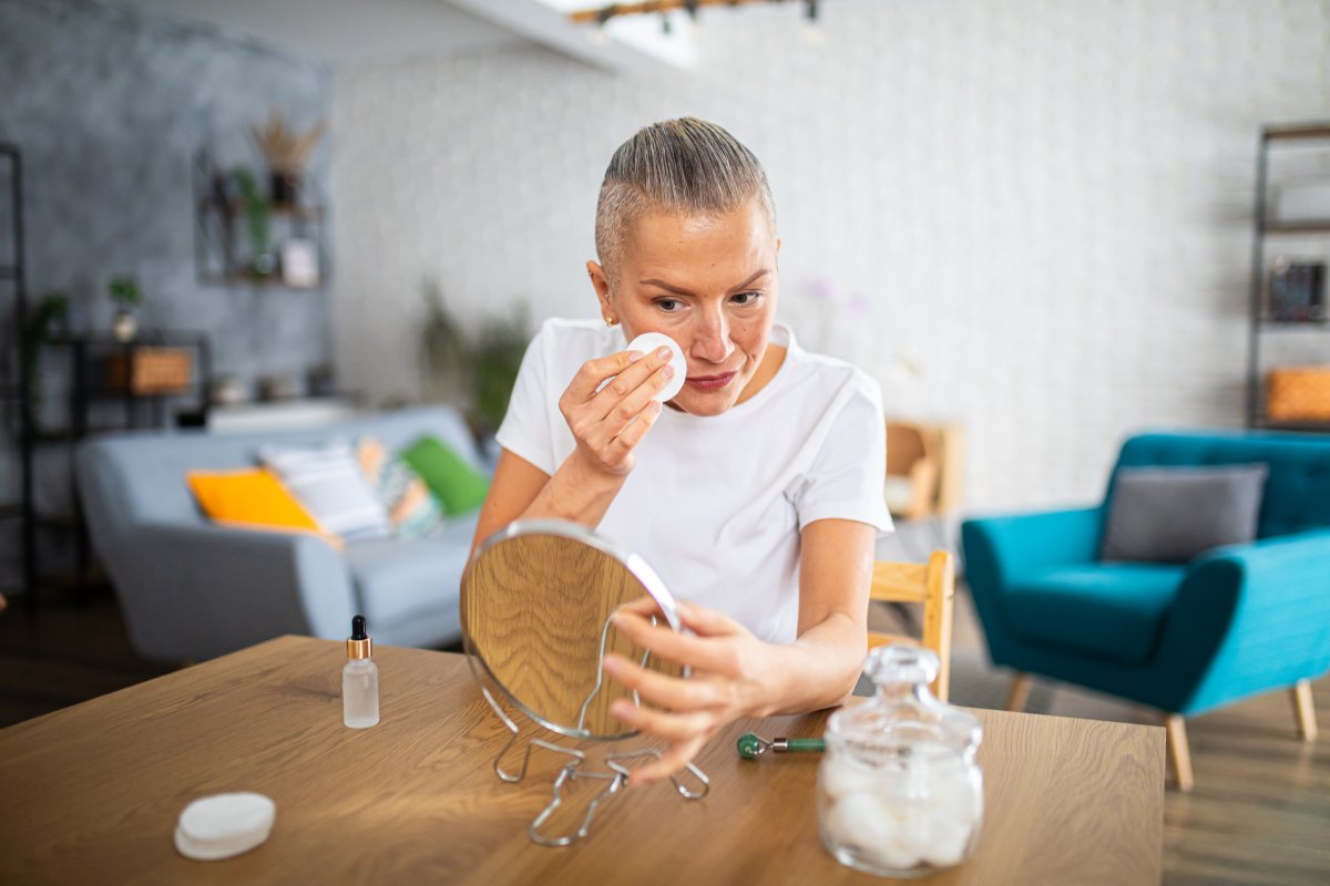 Happy middle-aged woman using a cotton pad for skin care at home