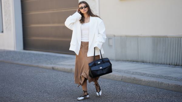 BERLIN, GERMANY - MAY 27: Lisa Mottl is seen wearing an off-white double-breasted oversized blazer with sharp wide peak lapels, padded shoulders, long sleeves, two parallel rows of matching fabric-covered buttons and classic horizontal flap pockets from Bazhane; a white fitted top from Zara; camel brown cargo-inspired cropped capri length trousers with belt loops, angled flap pockets, wide fluid legs and adjustable drawstring toggle hems creating a gathered balloon-like silhouette from Zara; off-white leather "Taekwondo Mei" ballet flats featuring iconic contrast black stripes, a flexible gum sole and delicate wrap-around ankle laces from Adidas; a black "Archive Gloria II Satchel L" large shoulder bag crafted from soft calf leather with a flap main compartment, an applied front pocket, twist lock closures, two top handles, side snap buttons for width adjustment and logo embossing on the front from Liebeskind Berlin; necklaces; "Olsen" sunglasses with a slim rectangular frame crafted from black acetate and smoke grey lenses from Vehla; her brown hair is worn loose with a center part; with natural make up on May 27, 2026 in Berlin, Germany. (Photo by Moritz Scholz/Getty Images)