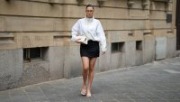 FRANKFURT AM MAIN, GERMANY - JUNE 4: Lea Cardenas is seen wearing a white technical fabric zip front jacket with a high stand collar, dropped shoulders, elasticated cuffs and an oversized silhouette from Under Armour; a black mini skirt with a fitted straight silhouette from NAKD Fashion; nude leather thong sandals with a square toe and low kitten heel from NAKD Fashion; a natural pedicure visible through the open toe sandal; a medium sized ivory leather top handle bag with a structured rectangular silhouette, silver tone hardware and folded side gusset detailing from Verafied; small silver stud earrings and a gold ring; rectangular acetate eyeglasses with clear lenses from Jimmy Fairly; her dark brown hair is styled in a sleek low bun with a center part; with natural make up on June 4, 2026 in Frankfurt am Main, Germany. (Photo by Moritz Scholz/Getty Images)