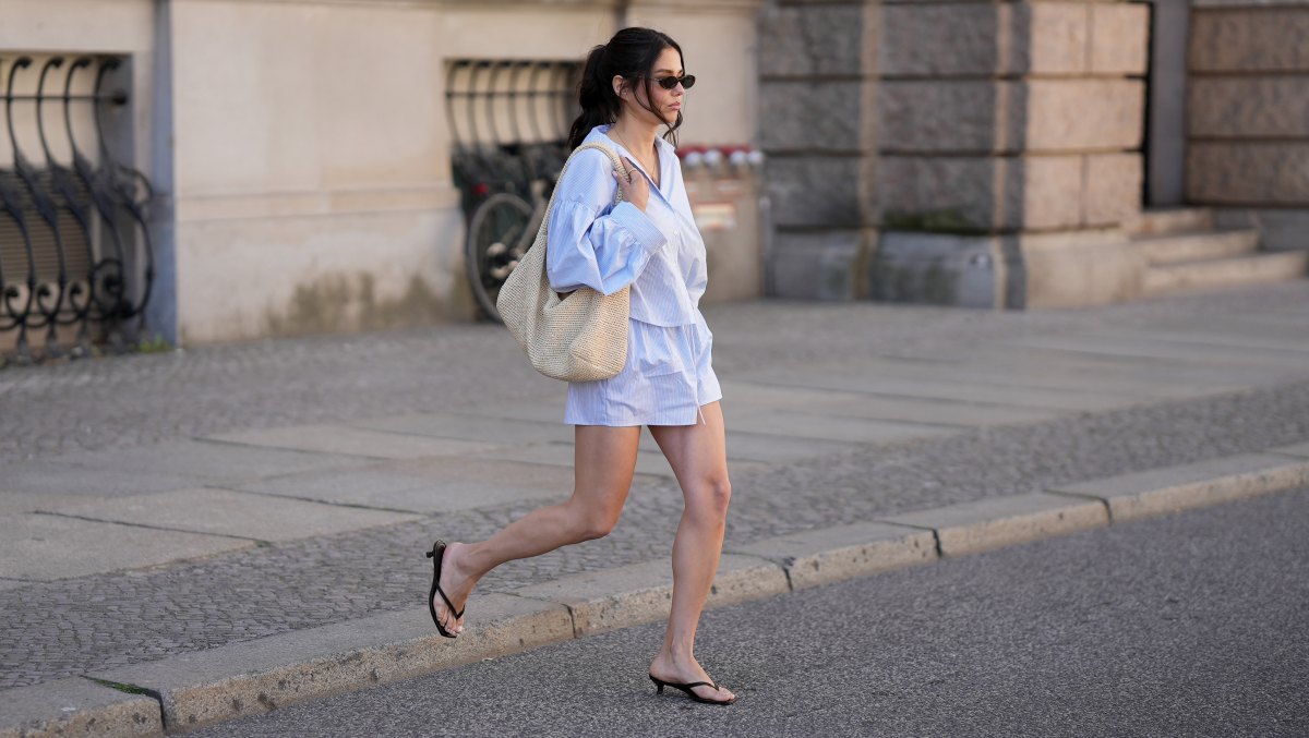 BERLIN, GERMANY - MAY 27: Aylin Sengül is seen wearing a blue-and-white striped oversized two-piece set consisting of a cropped button-up shirt with voluminous sleeves and matching shorts by Set Dish; black kitten-heel thong sandals by H&M; a large raffia shoulder bag by COS; narrow rectangular sunglasses by Chanel; gold jewelry consisting of rings and a delicate necklace; natural makeup; her dark brown hair is styled in a relaxed low updo with loose face-framing strands on May 27, 2026 in Berlin, Germany. (Photo by Moritz Scholz/Getty Images)
