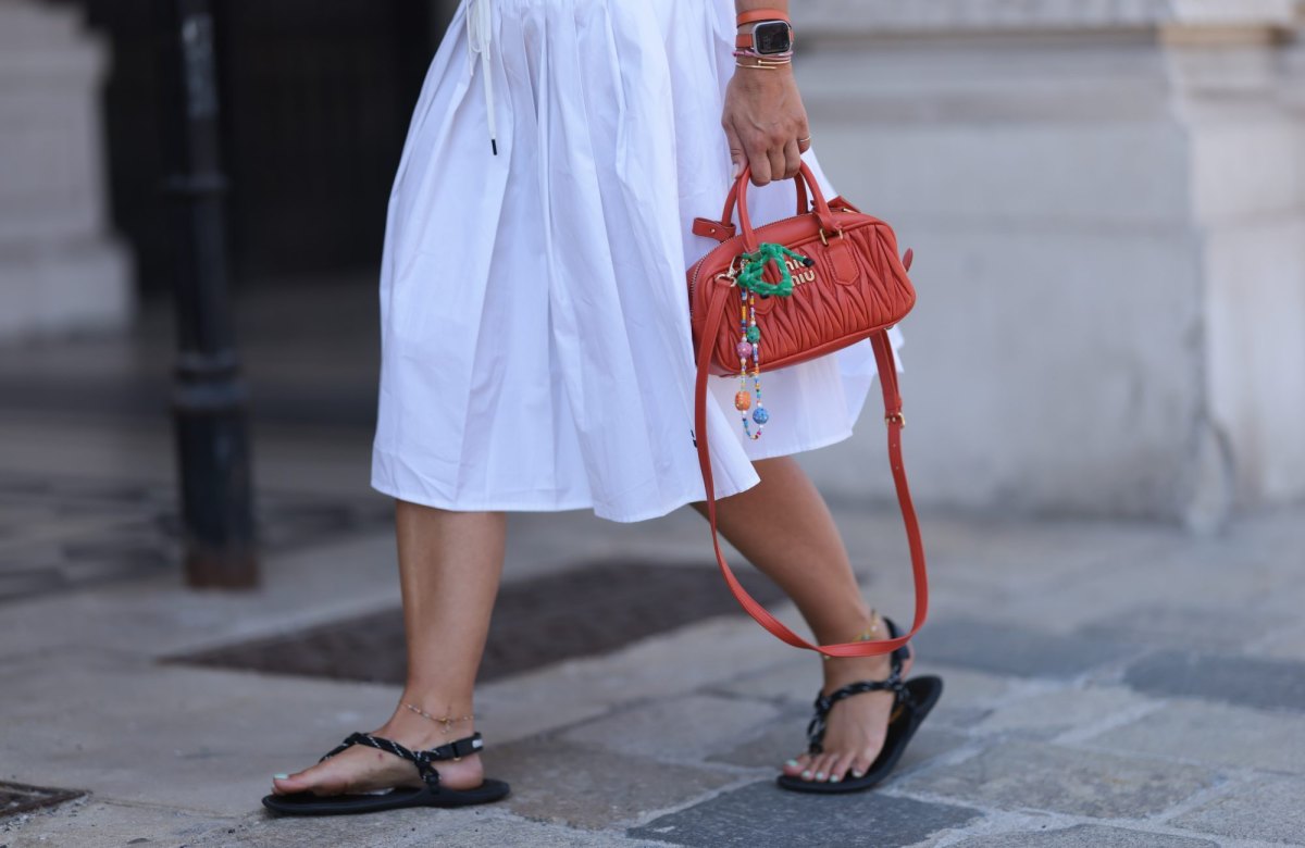 VIENNA, AUSTRIA - JULY 16: Karin Teigl is seen wearing several bracelets including the yellow-gold “Juste un Clou“ bracelet from Cartier; an Apple watch with orange leather bracelet; a white, pleated midi skirt from Miu Miu; an orange leather crossbody bag from Miu Miu with multi-color pearl chain pendant; black flip flops from Miu Miu; and two ankle chains on July 16, 2024 in Vienna, Austria. (Photo by Jeremy Moeller/Getty Images)