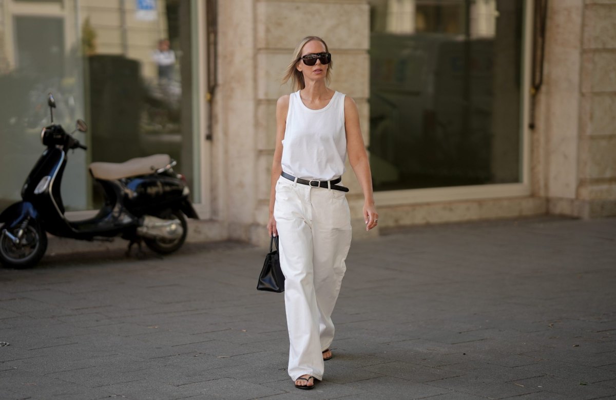 MUNICH, GERMANY - JUNE 15: Mirja Klein is seen wearing a white cotton sleeveless top with a relaxed silhouette from Frankie Shop; white cotton trousers with a wide leg silhouette from Remain Birger; a black leather belt with a metal buckle from Dehanche; black flat sandals from Massimo Dutti; a natural pedicure visible through the sandals; a black leather top handle bag with a compact silhouette from Shop the Curated; rings; rectangular acetate sunglasses with dark tinted lenses from Dolce & Gabbana; her blonde hair is worn loose with a straight texture; with natural make up on June 15, 2026 in Munich, Germany. (Photo by Moritz Scholz/Getty Images)