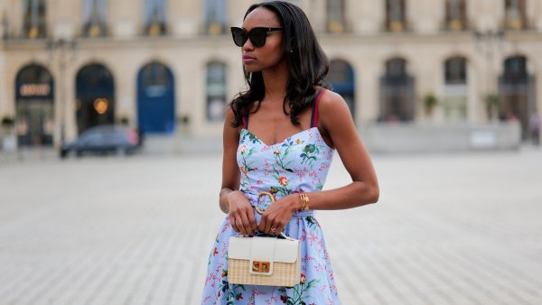 PARIS, FRANCE - APRIL 29: Emilie Joseph wears black large sunglasses, crystal earrings, a pale blue with red / green / navy blue / beige flower print pattern heart neck / tank-top / belted / midi dress, a beige wickers and white shiny leather bi-material handbag, during a street style fashion photo session, on April 29, 2023 in Paris, France. (Photo by Edward Berthelot/Getty Images)