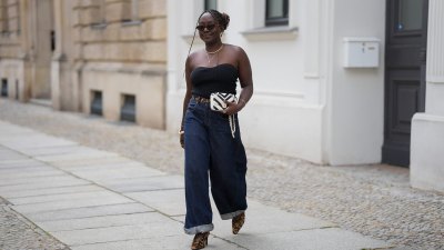 BERLIN, GERMANY - JULY 4: Lois Opoku is seen wearing a black ribbed strapless top with a sweetheart neckline from Uniqlo; dark blue high waist wide leg denim jeans with turned up cuffs from Levi’s; a slim leopard print belt from H&M Studio; leopard print pointed toe Mary Jane pumps from H&M Studio; a Chanel Mini CC bicolor chevron stitched lambskin flap shoulder bag with a gold tone chain strap; a gold collar necklace from Alexis Bittar and a gold pendant necklace from Bruna the Label; gold hoop earrings from ASOS; gold cuff bracelets and a gold chain bracelet from Petite Villa Mauresque; rings from Pandora and Maria Black; oval tortoiseshell frame sunglasses with dark tinted lenses from Corlin during the Berlin Fashion Week Spring/Summer 2026 on July 4, 2026 in Berlin, Germany. (Photo by Moritz Scholz/Getty Images)