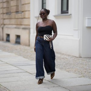 BERLIN, GERMANY - JULY 4: Lois Opoku is seen wearing a black ribbed strapless top with a sweetheart neckline from Uniqlo; dark blue high waist wide leg denim jeans with turned up cuffs from Levi’s; a slim leopard print belt from H&M Studio; leopard print pointed toe Mary Jane pumps from H&M Studio; a Chanel Mini CC bicolor chevron stitched lambskin flap shoulder bag with a gold tone chain strap; a gold collar necklace from Alexis Bittar and a gold pendant necklace from Bruna the Label; gold hoop earrings from ASOS; gold cuff bracelets and a gold chain bracelet from Petite Villa Mauresque; rings from Pandora and Maria Black; oval tortoiseshell frame sunglasses with dark tinted lenses from Corlin during the Berlin Fashion Week Spring/Summer 2026 on July 4, 2026 in Berlin, Germany. (Photo by Moritz Scholz/Getty Images)