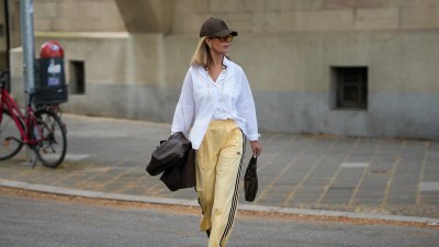 FRANKFURT AM MAIN, GERMANY - APRIL 21: Yvonne Schuppler-Kammerer is seen holding a dark brown leather blazer from Stradivarius; wearing an oversized white button down shirt from Zara; pale yellow wide leg track trousers with black three-stripe detail from Adidas; black pointed toe slingback pumps from H&M; a dark brown FF monogram canvas "Fendi Zucchino Half Moon Baguette Bag" from Fendi; a "Grace" gold wristwatch from Kapten & Son; a long pearl necklace from Zara; gold chunky hoop earrings and multiple gold rings from H&M and Scandivv; a nude manicure; oversized amber tinted square frame sunglasses from Bershka; a dark brown New York Yankees baseball cap from New Era; her blonde straight hair is worn loose; with natural make-up on April 21, 2026 in Frankfurt am Main, Germany. (Photo by Moritz Scholz/Getty Images)