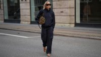 Mirja Klein is seen wearing a navy zip front jacket with a high collar from The Frankie Shop; matching navy cargo trousers with a self tie belt from The Frankie Shop; brown leather flip flops from A.Emery; a medium sized olive suede top handle bag from DeMellier; oversized rectangular acetate sunglasses with dark tinted lenses from Phoebe Philo; blonde hair worn long with a center part during the Copenhagen Fashion Week Spring/Summer 2027 on August 6, 2026 in Copenhagen, Denmark.