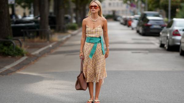 Julia Kammerer is seen wearing a beige plaid midi dress from Mango; a wide turquoise fabric belt from Mango; beige flip flops from Ulanka; a large brown leather tote bag with gold tone hardware from DeMellier; layered pearl and gold chain necklaces from Chanel and Akind & Scandiv, gold hoop earrings, rings from Pandora, Scandiv and Akind, gold bracelets and a silver and gold tone watch from Mockberg; oversized translucent acetate sunglasses with brown tinted lenses from & Other Stories; blonde hair worn straight with a center part on August 7, 2026 in Frankfurt am Main, Germany.