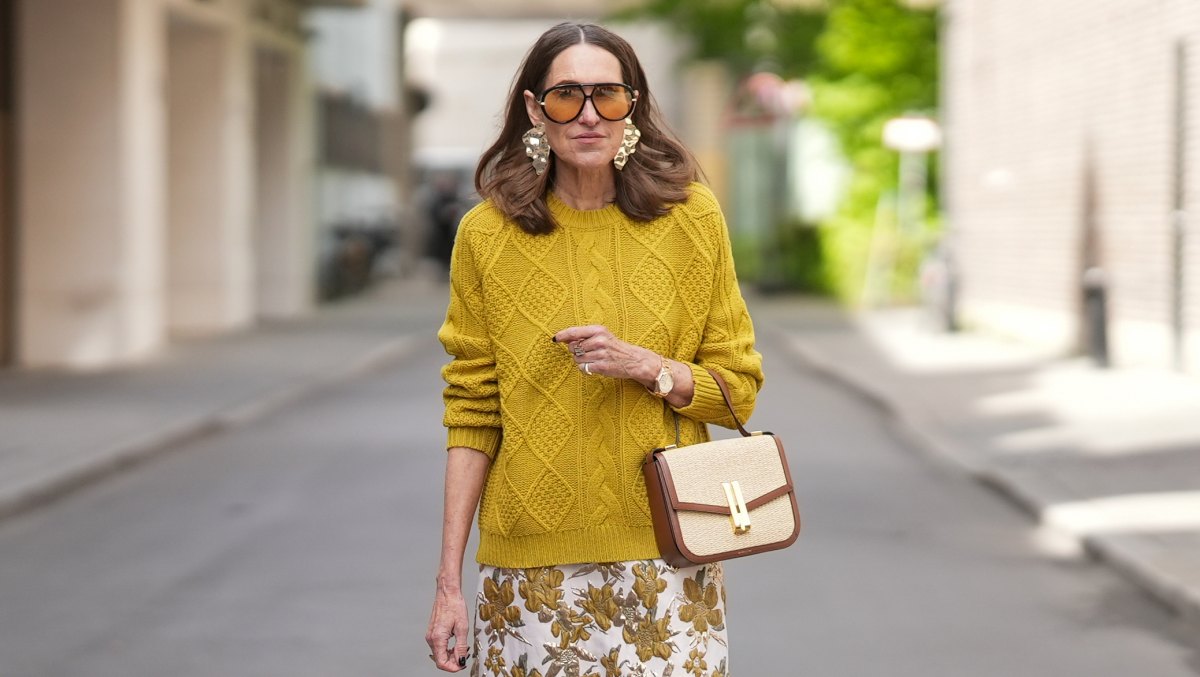 MUNICH, GERMANY - APRIL 28: Annette Weber is seen wearing a mustard yellow wool knit sweater with a relaxed fit, ribbed crew neck, cuffs and hem and cable knit texture from Allude; a white cotton midi skirt with a straight silhouette and gold and brown floral print from TT Stories; a medium sized beige raffia and brown leather “Vancouver” shoulder bag with envelope flap top, double bar gold toned lock from DeMellier; gold tone statement drop earrings, a Rolex Day-Date 36 Everose rose gold with Oyster bracelet; multiple gold rings; dark nail polish; oversized aviator acetate sunglasses with orange tinted lenses from Bottega Veneta; her medium brown hair is worn loose in soft waves with a center part; with natural make up on April 28, 2026 in Munich, Germany. (Photo by Moritz Scholz/Getty Images)