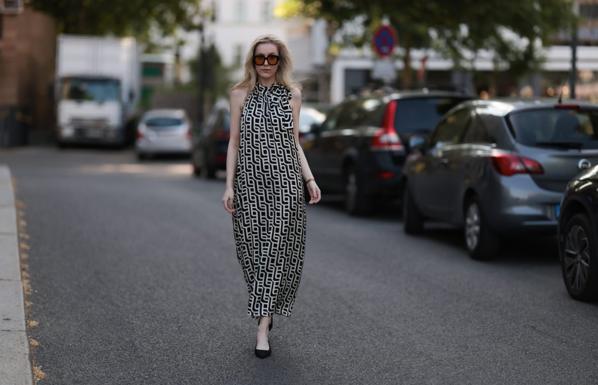 BERLIN, GERMANY - JUNE 19: Lil Paulin is seen wearing oversized black square-framed sunglasses with orange lenses and wide temples, gold hoop earrings, a flowy sleeveless maxi dress with a halter neck and a geometric black and white pattern, a gold rectangular watch from Daniel Wellington, several filigree silver rings, and pointed black suede slingback kitten heels on June 19, 2025 in Berlin, Germany. (Photo by Jeremy Moeller/Getty Images)