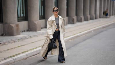 COPENHAGEN, DENMARK - AUGUST 3: Sophia Geiss is seen wearing a beige oversized double breasted cotton trench coat with wide lapels, epaulettes, storm flap, adjustable cuff straps and a self tie belt from H&M; a grey fitted crewneck T shirt from Brandy Melville; dark indigo wide leg jeans from Acne Studios; black leather minimalist open toe flat sandals from Mango; a black leather structured top handle tote bag from COS; oversized black shield sunglasses with a bold acetate frame from Tom Ford during the Copenhagen Fashion Week Spring/Summer 2027 on August 3, 2026 in Copenhagen, Denmark. (Photo by Moritz Scholz/Getty Images)