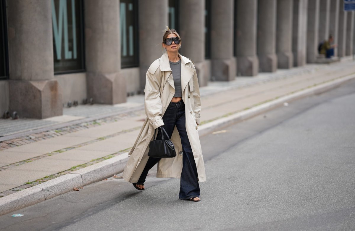 COPENHAGEN, DENMARK - AUGUST 3: Sophia Geiss is seen wearing a beige oversized double breasted cotton trench coat with wide lapels, epaulettes, storm flap, adjustable cuff straps and a self tie belt from H&M; a grey fitted crewneck T shirt from Brandy Melville; dark indigo wide leg jeans from Acne Studios; black leather minimalist open toe flat sandals from Mango; a black leather structured top handle tote bag from COS; oversized black shield sunglasses with a bold acetate frame from Tom Ford during the Copenhagen Fashion Week Spring/Summer 2027 on August 3, 2026 in Copenhagen, Denmark. (Photo by Moritz Scholz/Getty Images)