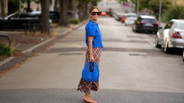 FRANKFURT AM MAIN, GERMANY - AUGUST 7: Yvonne Schuppler-Kammerer is seen wearing a bright blue short sleeve collared top with a tie waist from Zara; a brown and blue checked midi skirt from Mango; beige leather flat sandals from Mango; a small blue suede bag from Mango; gold hoop earrings, a gold bracelet; oversized tortoiseshell frame sunglasses with dark tinted lenses from Gina Tricot; brown hair worn in a sleek low bun on August 7, 2026 in Frankfurt am Main, Germany. (Photo by Moritz Scholz/Getty Images)