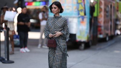 Heart Evangelista is seen wearing golden earrings, a white/black/brown houndstooth patterned nigh neck midi dress with puffy long-sleeves, a golden watch, several rings in silver and gold, a purple leather bag from Carolina Herrera and plateau ankle boots in golden suede with floral print and chunky silber heels outside before the Carolina Herrera Spring Summer 2024 Runway Show on September 12, 2023 in New York City.
