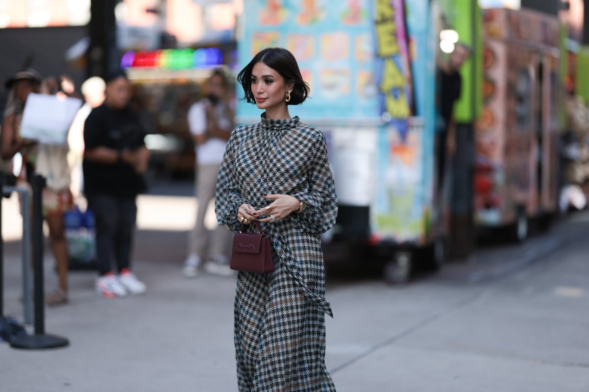 Heart Evangelista is seen wearing golden earrings, a white/black/brown houndstooth patterned nigh neck midi dress with puffy long-sleeves, a golden watch, several rings in silver and gold, a purple leather bag from Carolina Herrera and plateau ankle boots in golden suede with floral print and chunky silber heels outside before the Carolina Herrera Spring Summer 2024 Runway Show on September 12, 2023 in New York City.