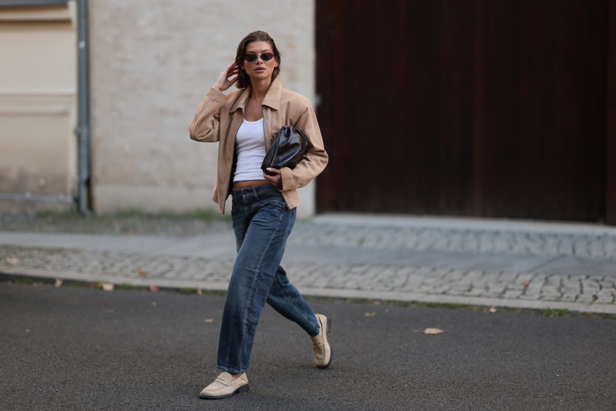 Sophia Geiss seen wearing Vehla Eyewear narrow oval-shaped black sunglasses with sleek frames, crisp white scoop-neck cotton basic tank top, The Worn cropped beige suede vintage jacket with a structured collar and relaxed sleeves, Cambio straight-leg mid-wash slightly loose denim jeans, The Frankie Shop black small leather drawstring bag with a glossy finish and Camper beige suede leather loafers, on September 06, 2025 in Berlin, Germany.