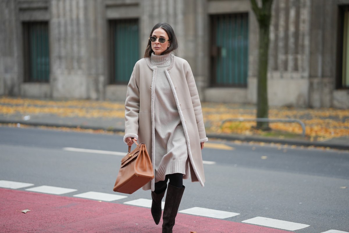 Patricia Wirschke is seen wearing a beige shearling coat with fur-trimmed edges and a straight silhouette by Manzoni 24; a light beige ribbed cashmere turtleneck dress by Incentive; black tights; dark brown suede knee-high boots with a pointed toe by Massimo Dutti; a camel brown leather “Kelly 32” handbag with gold hardware by Hermès; oval metal-frame sunglasses called “Triomphe Metal 01” by Céline; her brown hair is worn straight with a middle part on November 10, 2025 in Duesseldorf, Germany.