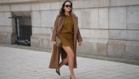 Laura Noltemeyer is seen wearing a a long camel-colored brushed wool coat with a wrap silhouette and integrated belt by Max Mara; a mustard-colored knit cardigan with a brushed cable-knit pattern and front button fastening by Sézane; a mustard yellow brownish mini skirt in a soft wool fabric by Sézane; black patent leather slingback pumps with a sharply pointed toe and silver hardware accents by Yves Saint Laurent; a small quilted tweed flap bag in a khaki Color with woven fabric material with a gold chain strap and CC clasp by Chanel; gold statement earrings with a ruffled surface and a green stone element by Mango; black cat eye sunglasses with an acetate frame by Yves Saint Laurent; her brown hair is styled in loose waves with a center part on November 13, 2025 in Hamburg, Germany.