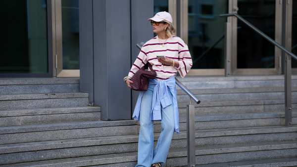 FRANKFURT AM MAIN, GERMANY - MARCH 26: Julia Kammerer is seen wearing an oversized pink and burgundy horizontal striped cotton T shirt from H&M; a blue and white striped button down shirt tied around her waist from JJXX; light blue wide leg denim jeans with a relaxed fit from JJXX; burgundy and yellow textured leather lace up sneakers from Adidas; a large burgundy woven leather hobo bag from NA-KD; a pale pink baseball cap with the red embroidered text "Amore a Milano" from LeGer by Lena Gercke; her jewelry includes chunky gold hoop earrings, necklaces and gold tone stacked rings worn across multiple fingers from H&M, Pandora and My Jewellery; holding an iPhone from Apple; several silver and resin bangles from & Other Stories; orange tinted aviator sunglasses with a thin black frame from Bershka; her blonde hair is styled in loose waves underneath the cap on March 26, 2026 in Frankfurt am Main, Germany. (Photo by Moritz Scholz/Getty Images)