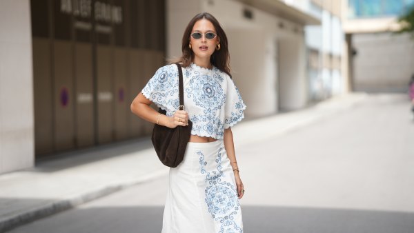 MUNICH, GERMANY - JUNE 16: Amanda Mühle is seen wearing a white cropped blouse with blue embroidered motifs, wide short sleeves and scalloped edges from Sézane; a white high waist midi skirt with blue embroidered motifs from Sézane; a dark brown suede shoulder bag with an adjustable strap and gold tone hardware from Rouje; gold hoop earrings, gold bracelets and gold rings; oval metal frame sunglasses with dark tinted lenses from Jimmy Fairly on June 16, 2026 in Munich, Germany. (Photo by Moritz Scholz/Getty Images)