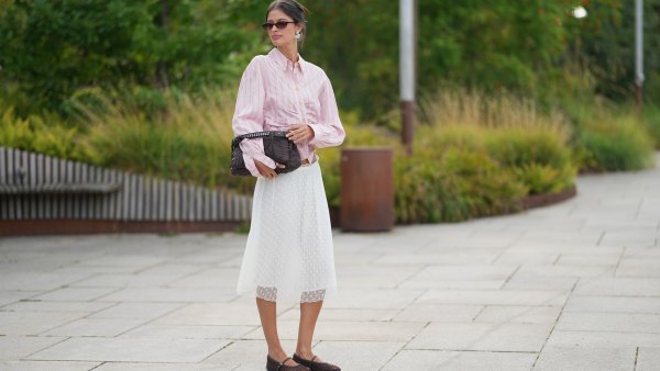A guest wears dark brown hair in a low bun, brown rectangular sunglasses with dark lenses, a pink and white striped button-through shirt with a spread collar and long sleeves tied at the waist, a white pleated midi skirt with white polka dot, a purple quilted leather clutch bag, brown woven mary jane flats shoes, outside Collina Strada, during Copenhagen Fashion Week Spring/Summer 2027, on July 06, 2026 in Copenhagen, Denmark