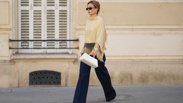 PARIS, FRANCE - AUGUST 17: Merve Gorgoz wears brown hair tied back with hair part, sunglasses, a beige yellow and white floral patterned vintage shawl with long knotted fringe, dark blue high-waisted wide-leg jeans denim pants by Sezane, a structured white handbag by Verafied, brown pointed-toe heels shoes by Jimmy Choo, during a street style fashion photo session, on August 17, 2026 in Paris, France. (Photo by Edward Berthelot/Getty Images)