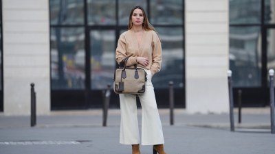 PARIS, FRANCE - FEBRUARY 09: Maria Rosaria Rizzo wears long brown hair, lipstick, earrings, a gray canvas Prada bag with brown leather trim, a beige knit V-neck cardigan, white straight-leg pants, brown suede boots shoes with a block heel, during a street style fashion photo session, on February 09, 2026 in Paris, France (Photo by Edward Berthelot/Getty Images)