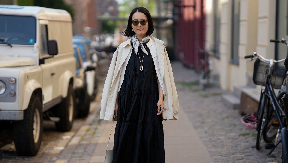 COPENHAGEN, DENMARK - AUGUST 3: A guest is seen wearing a black tiered midi dress layered with an off-white jacket draped over the shoulders, a printed silk neck scarf, cream shoulder bag, black leather fisherman sandals with cream socks, and tinted sunglasses outside the Frama Breakfast during Copenhagen Fashion Week Spring/Summer 2027 on August 3, 2026 in Copenhagen, Denmark. (Photo by Moritz Scholz/Getty Images)